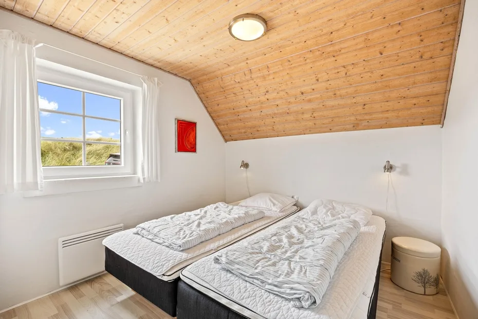 A bedroom with two beds beneath a sloped wooden ceiling and a window.
