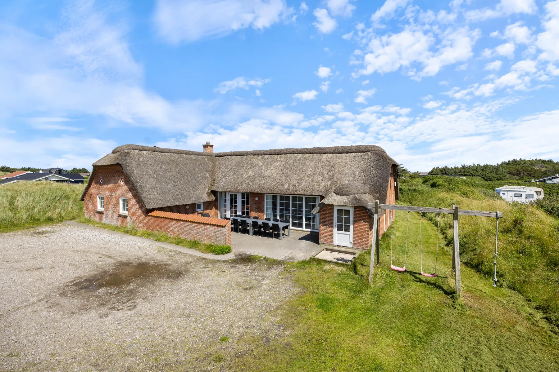 A thatched house stands beside a gravel drive and grassy yard.