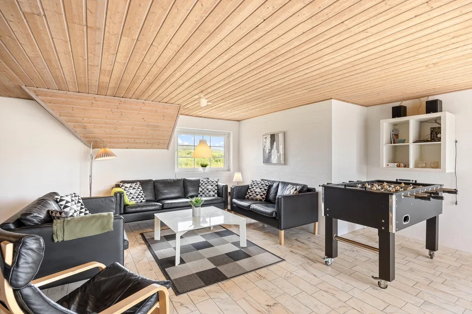 A bright living room with dark seating, a coffee table, and a foosball table.