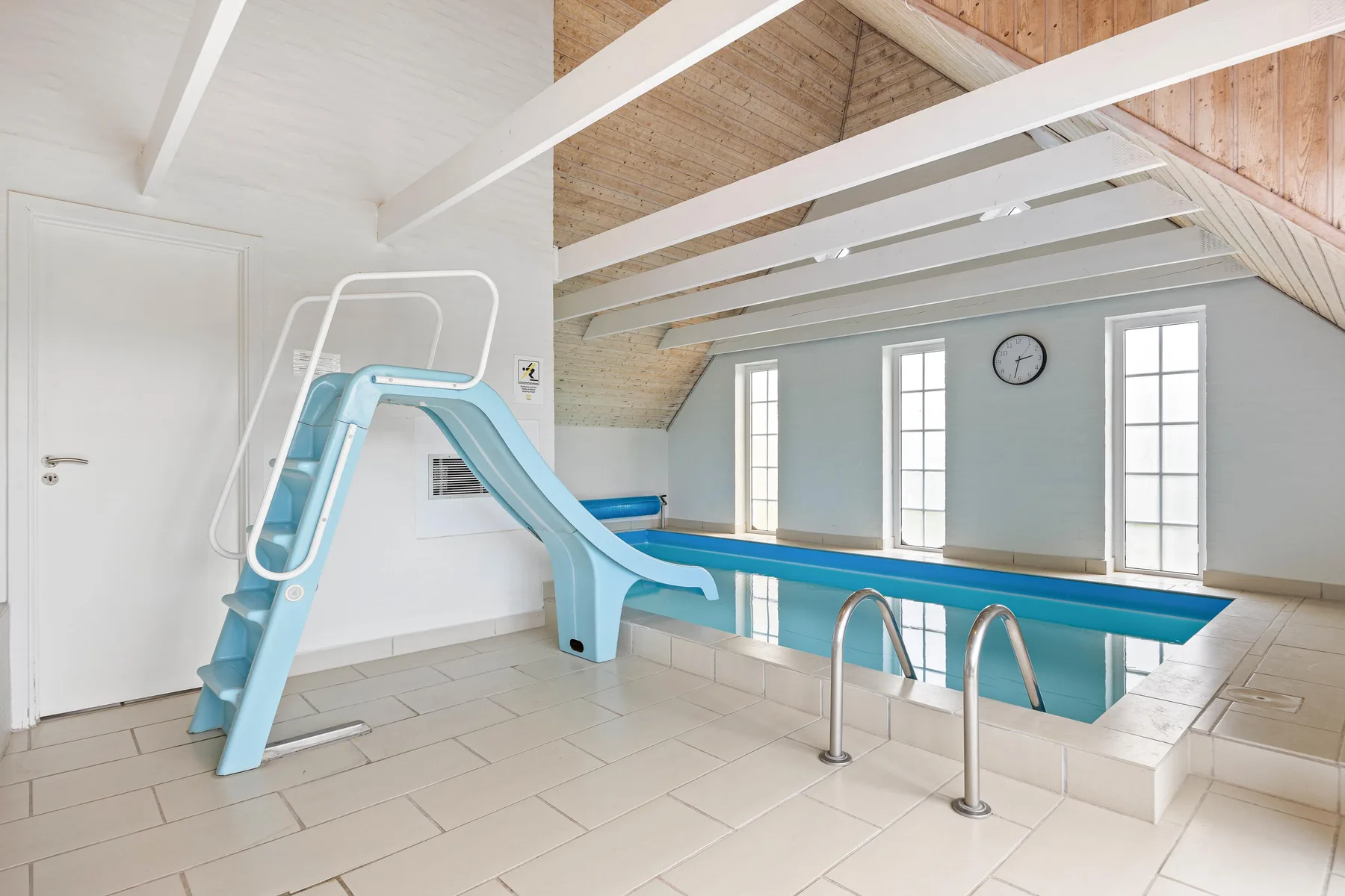 An indoor swimming pool beneath a sloped ceiling, with a blue water slide.