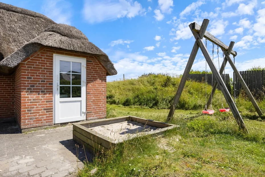 A small brick outbuilding stands beside a wooden swing set in a grassy yard.