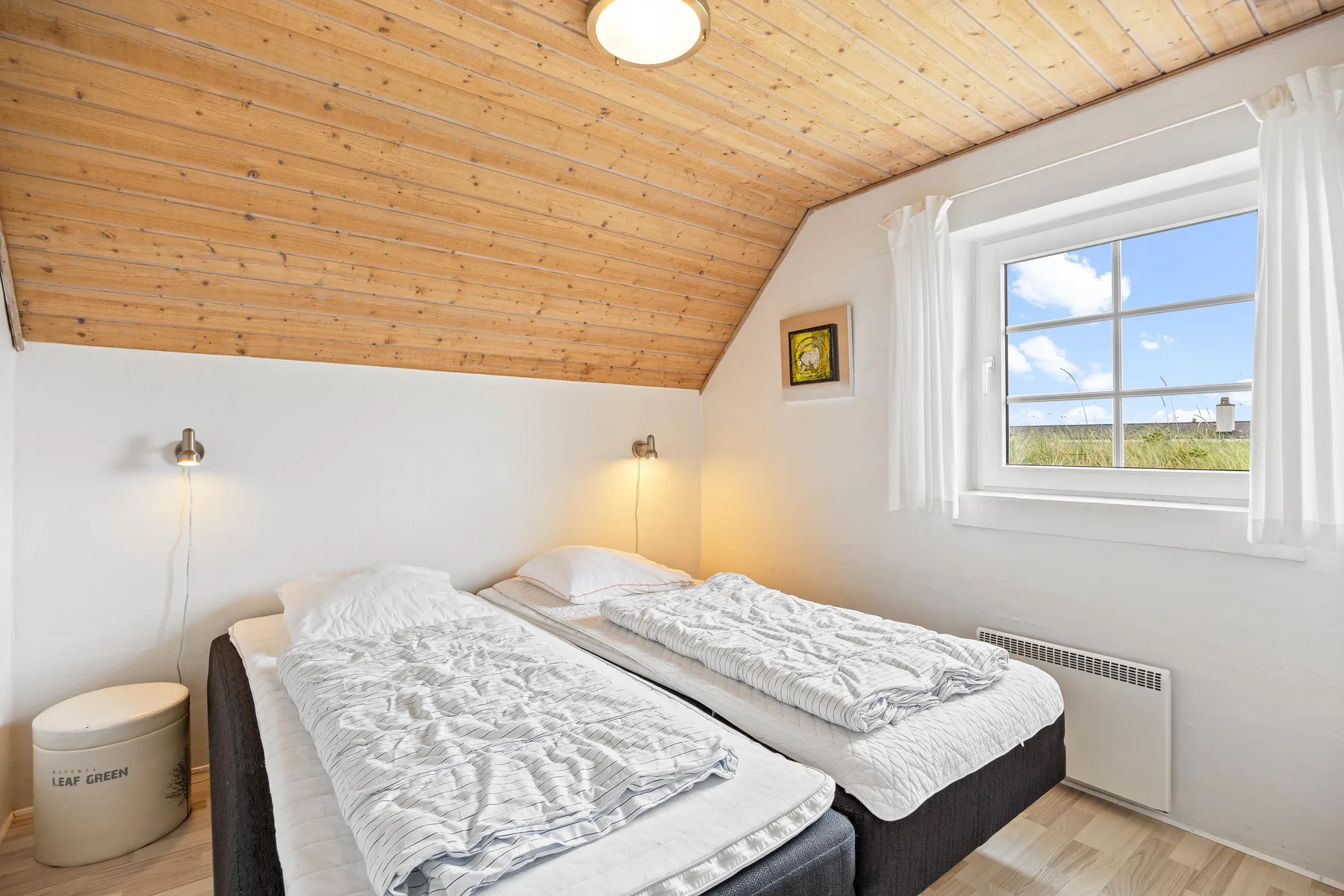 A bright bedroom with two beds beneath a sloped wood ceiling.