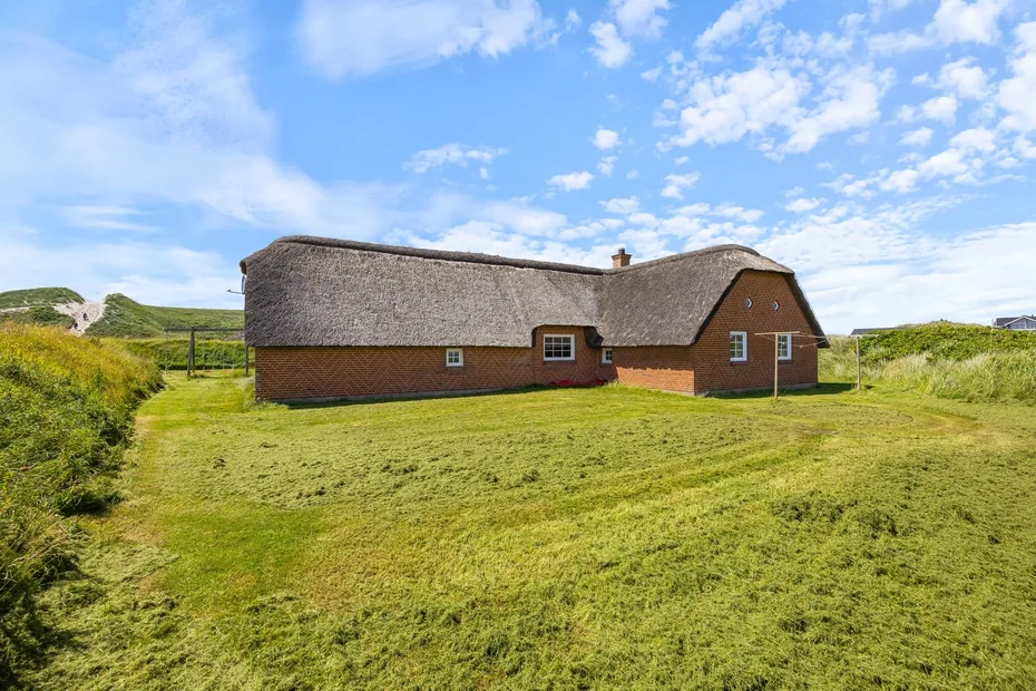 A thatched brick house stands amid a broad grassy lawn.