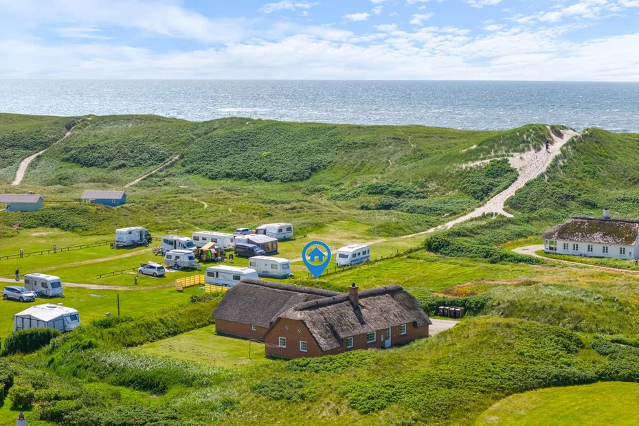 A thatched-roof building sits among grassy dunes, with the sea visible in the distance.
