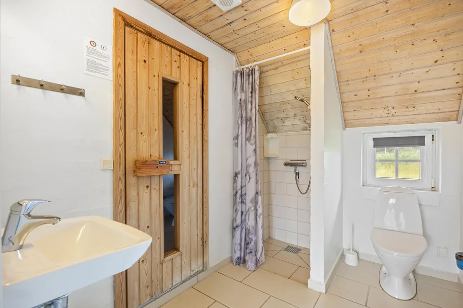 A tiled bathroom with a wooden sauna, shower, sink, and toilet.