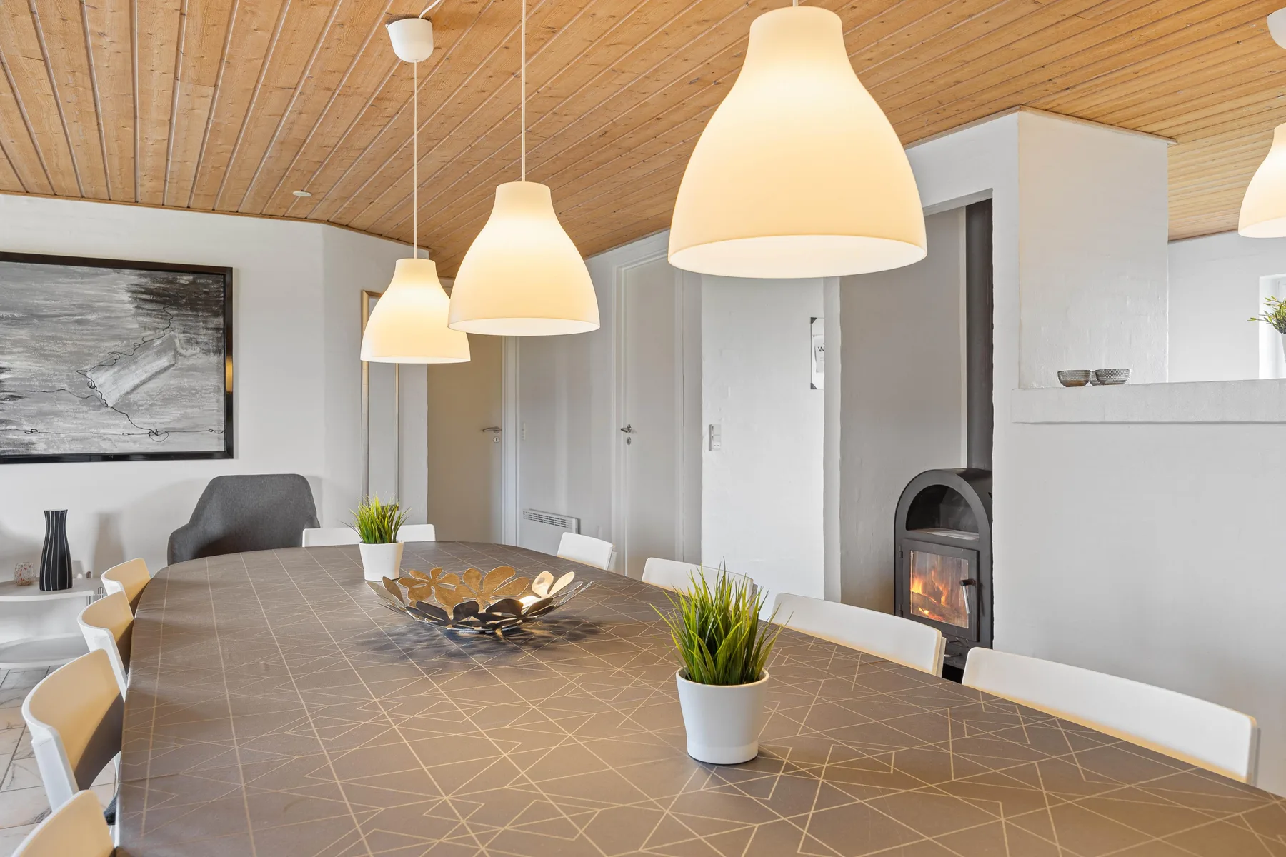 A dining area with a long table, pendant lights, and a fireplace.