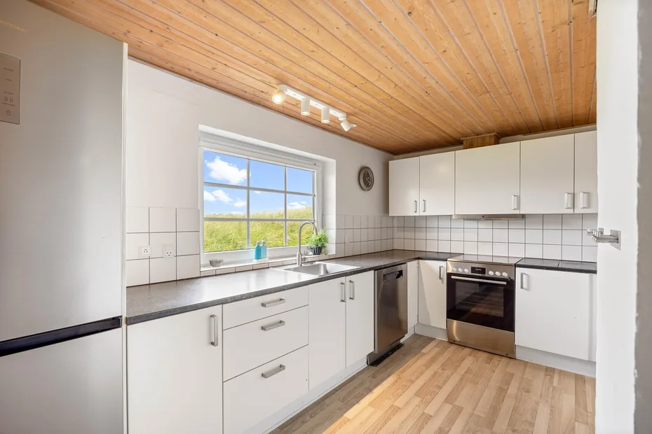 A bright kitchen with white cabinets, dark countertops, and a window.