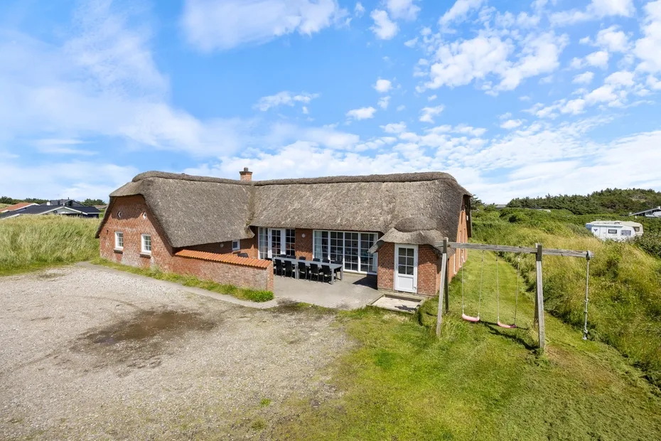 A thatched-roof brick building stands beside a gravel drive and grassy field.