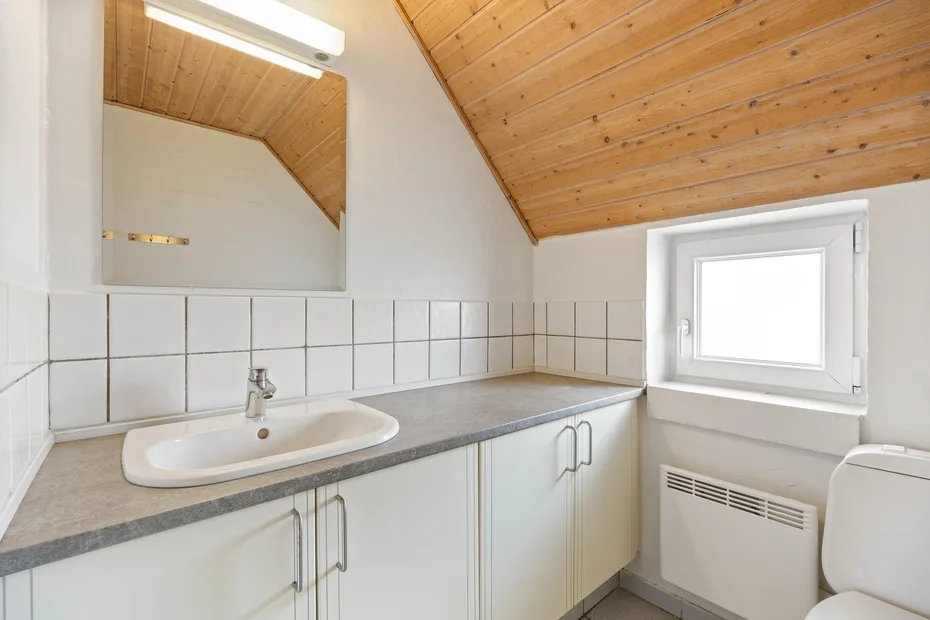 A bathroom vanity with a sink sits beneath a sloped wooden ceiling.