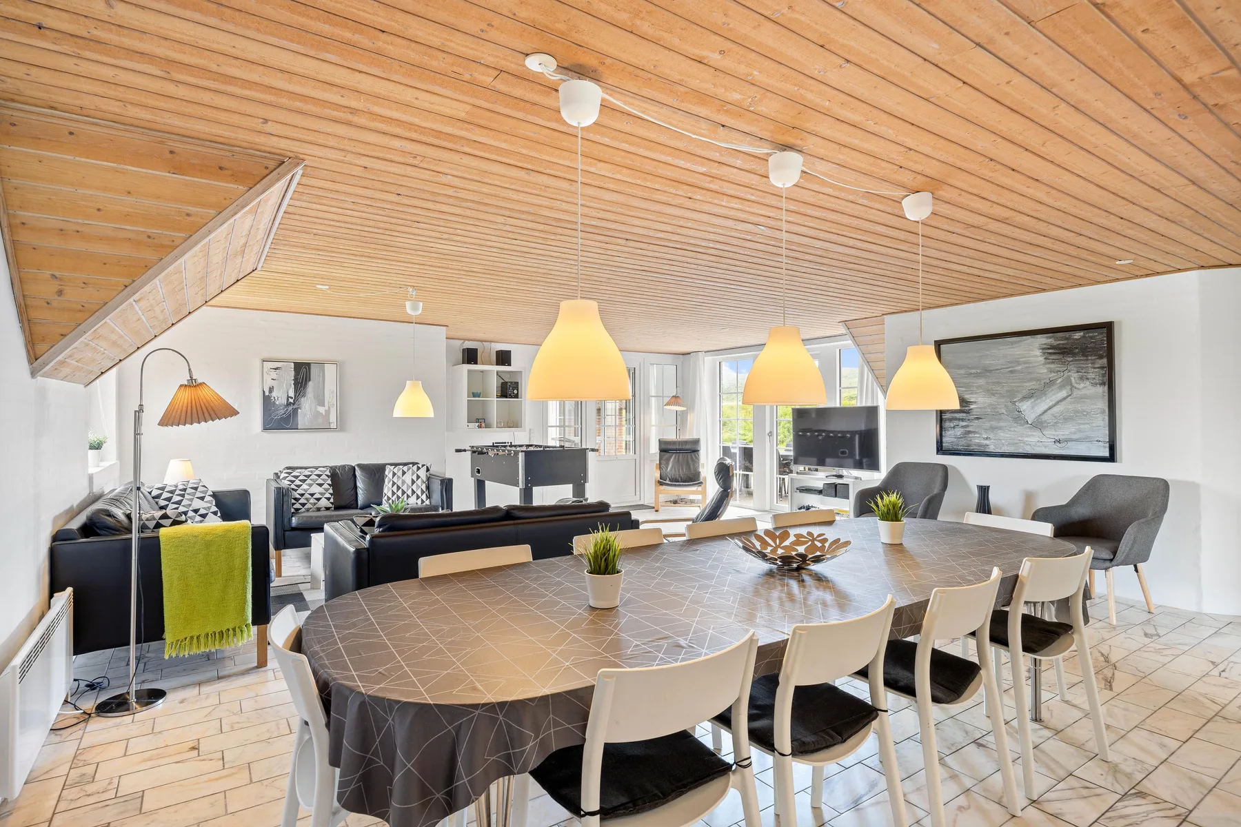 A dining area with a long table and seating opens onto a living room.