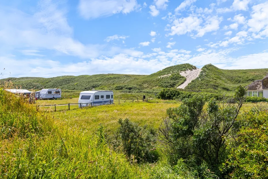 A grassy campsite with several caravans sits beneath rolling green hills.