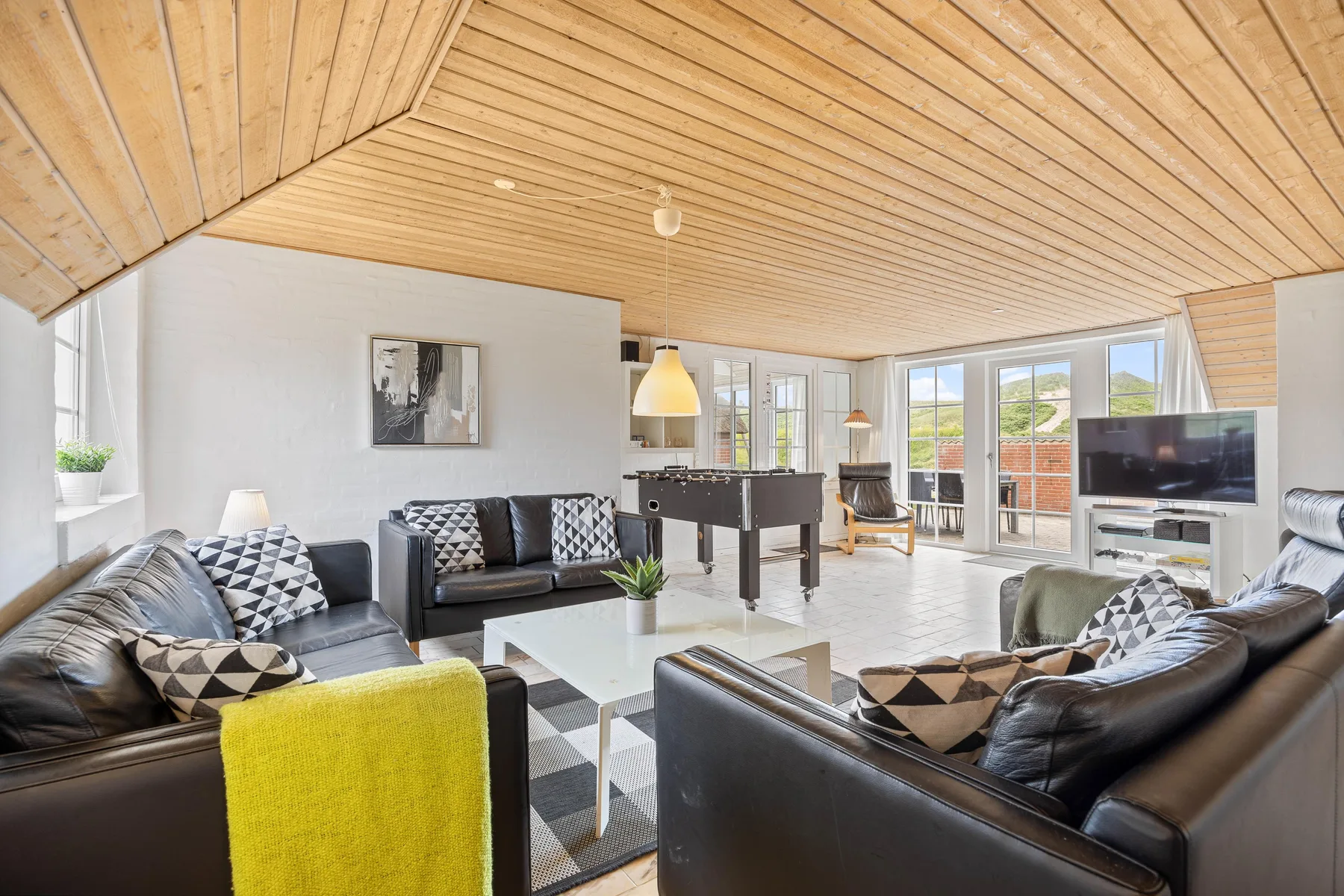 A bright living room with seating, a television, and large windows opening onto a patio.