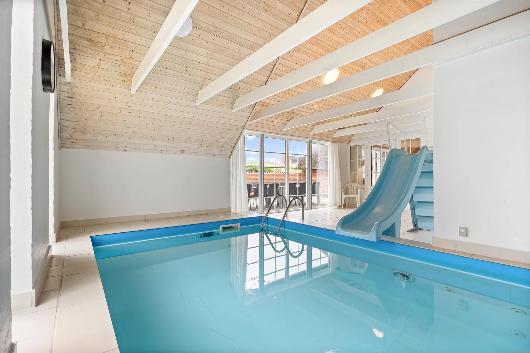An indoor swimming pool with a blue water slide beneath a sloped wooden ceiling.