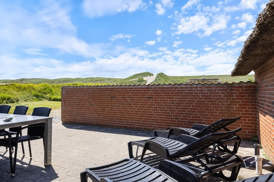 A paved outdoor terrace with lounge seating and a low brick wall.