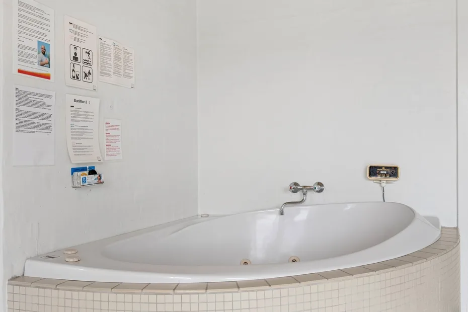 A bathroom with a large white bathtub beneath wall notices.