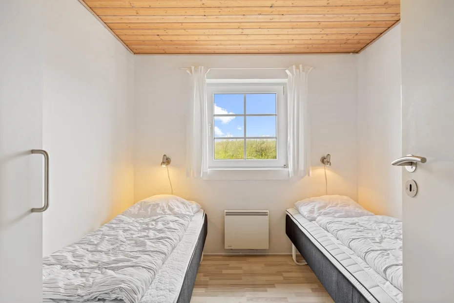 A bright bedroom with two single beds and a window overlooking greenery.