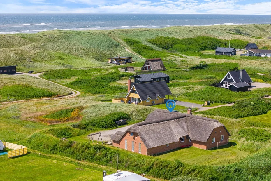 Aerial view of cottages among green dunes near the coastline.