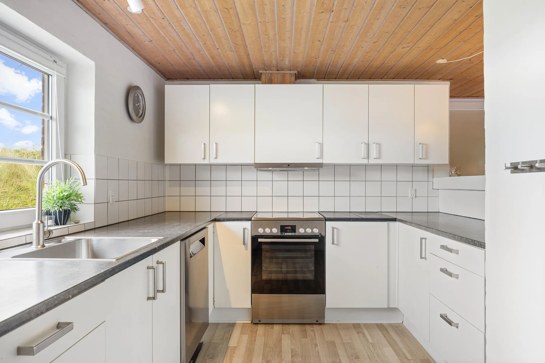 A bright kitchen with white cabinets, stainless-steel counters, and a window above the sink.