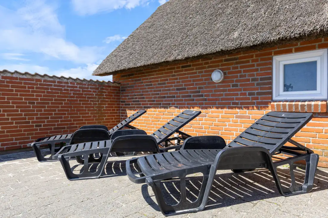 Outdoor patio with reclining lounge chairs beside a brick wall.