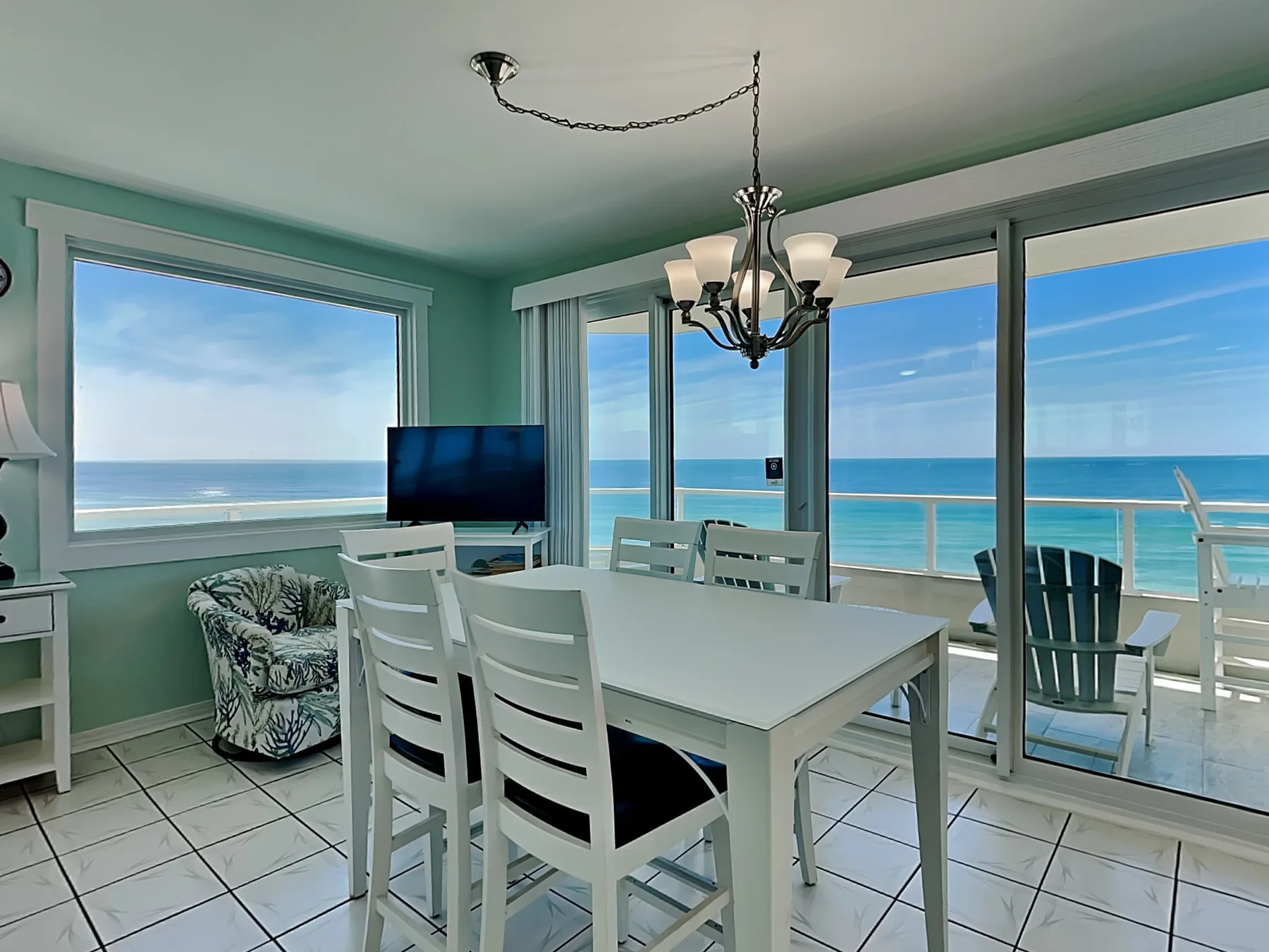 A dining area with a white table beside large windows overlooking the ocean.