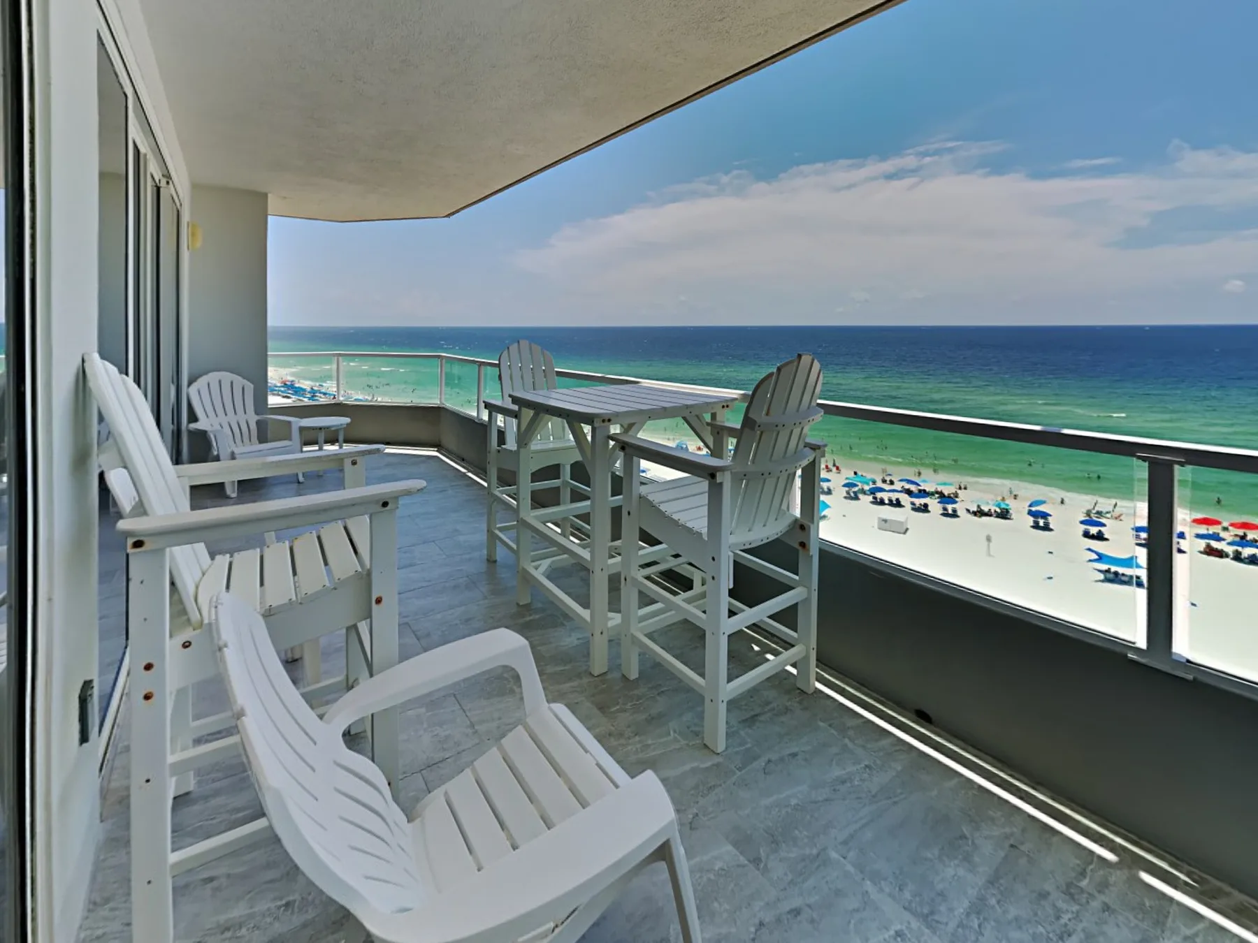 A covered balcony with white seating overlooks the beach and ocean.