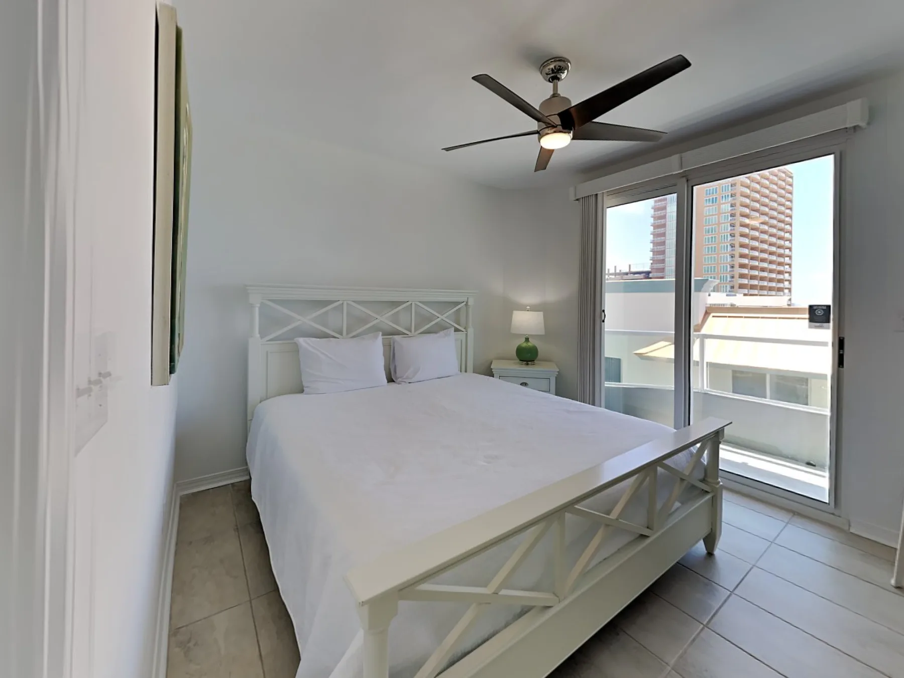 A bright bedroom with a white bed and sliding glass doors opening onto a balcony.