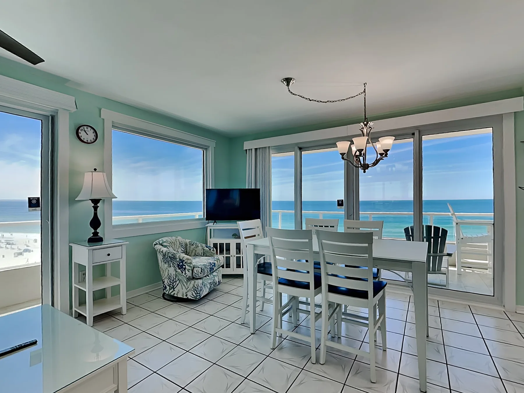 A bright dining area with a table and chairs beside wide windows overlooking the ocean.
