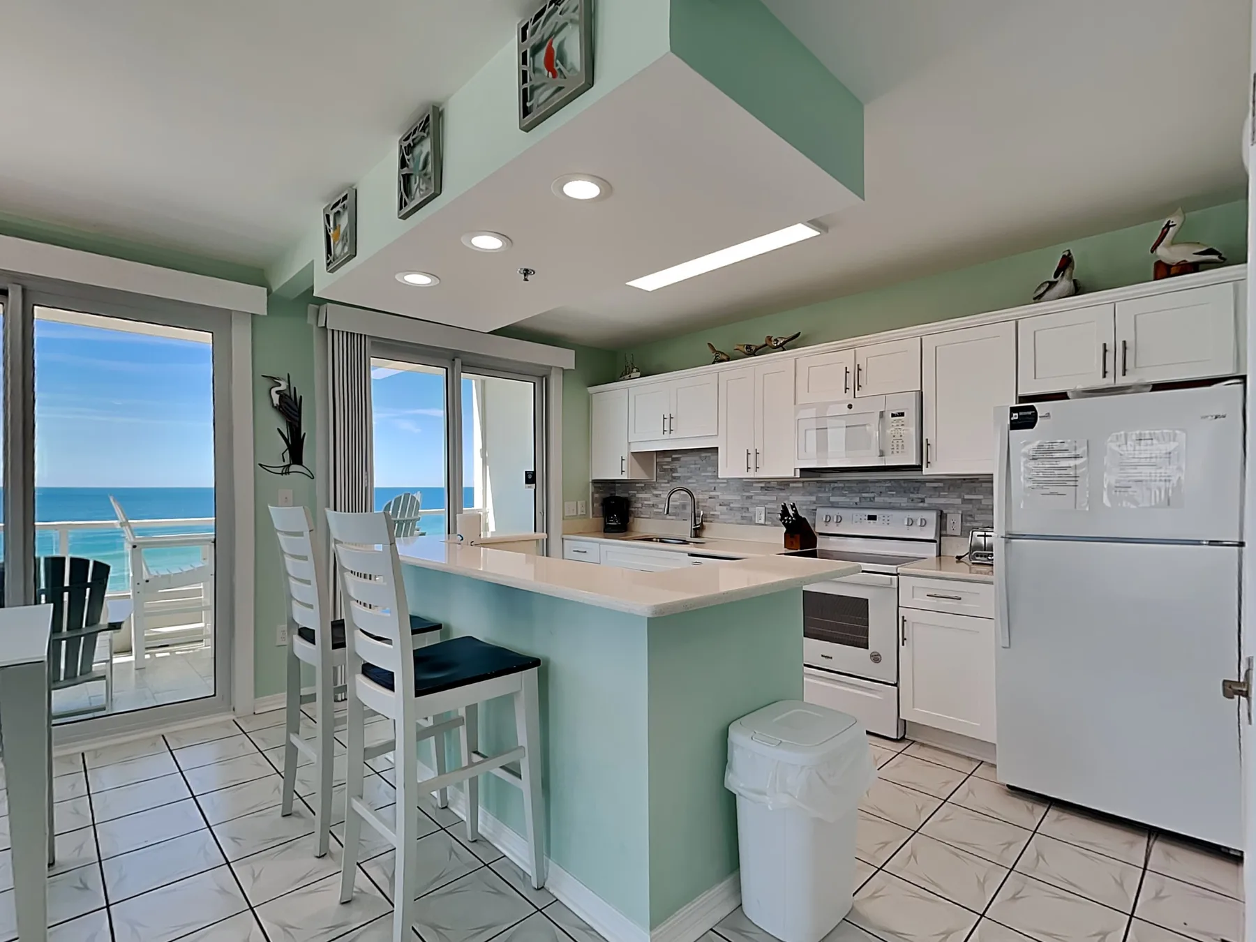 A bright kitchen with a mint-green island and sliding glass doors overlooking the sea.