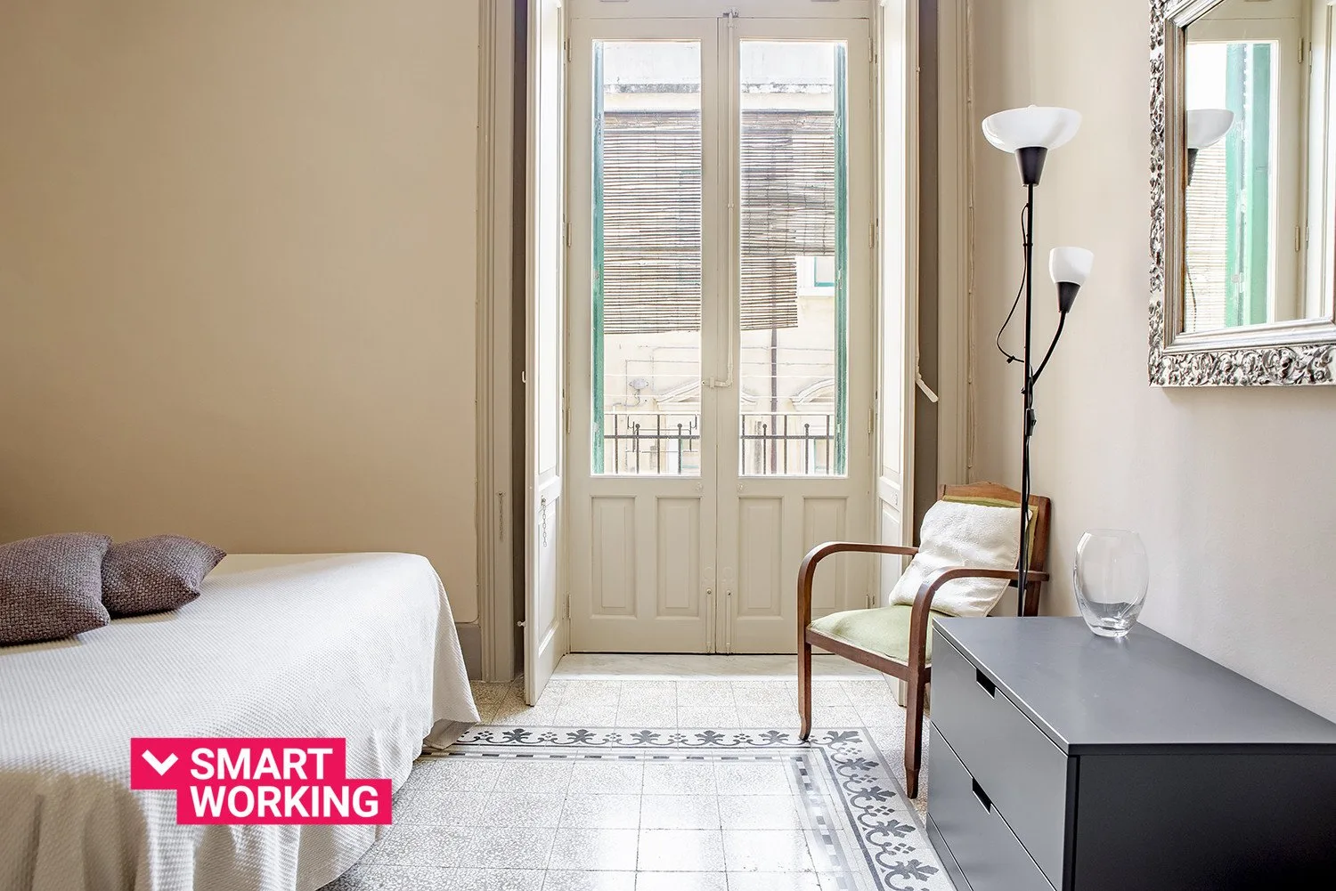 Un dormitorio luminoso con una cama, un sillón y puertas acristaladas que dan a un balcón.