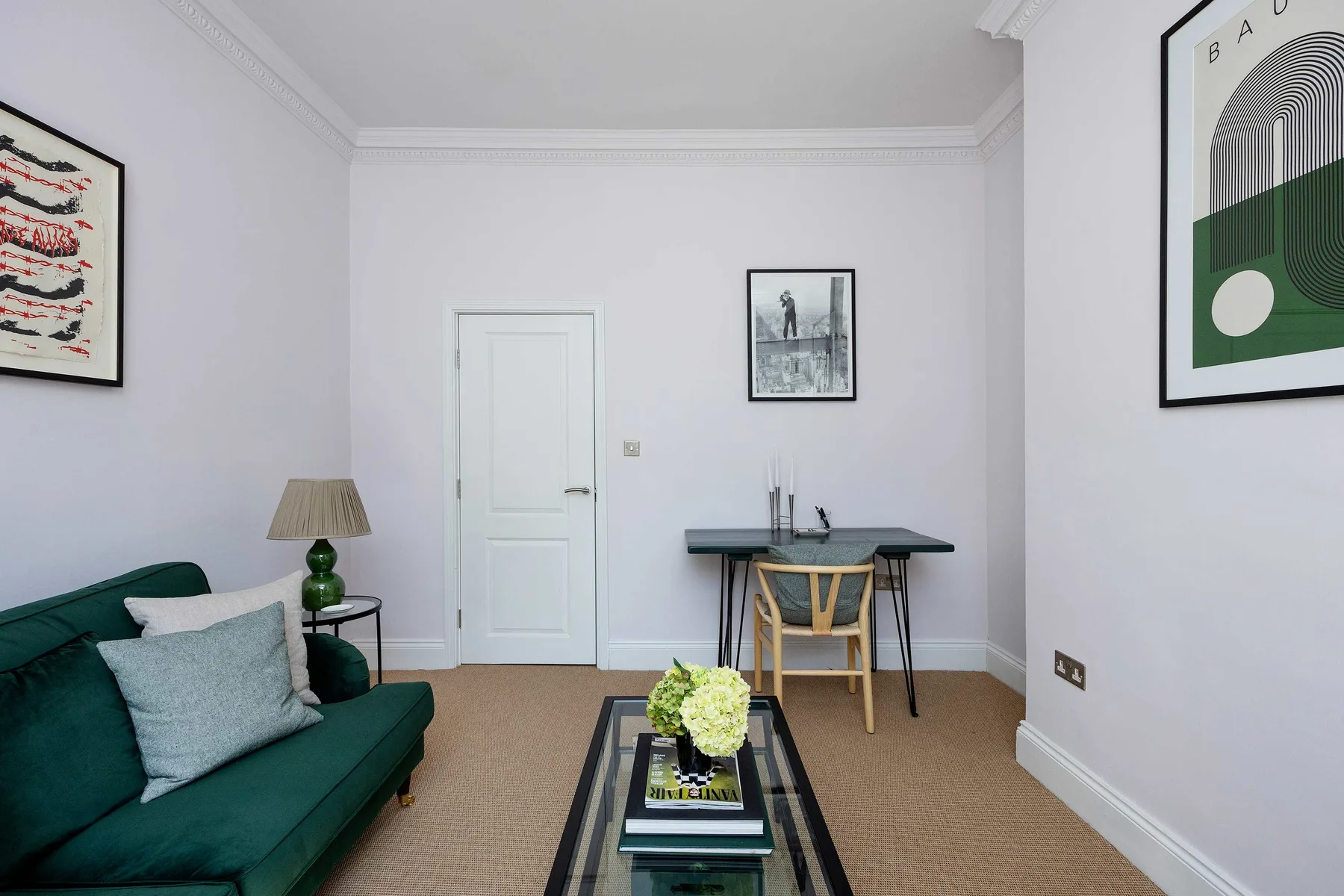A living room with green seating, a desk, and framed artwork.