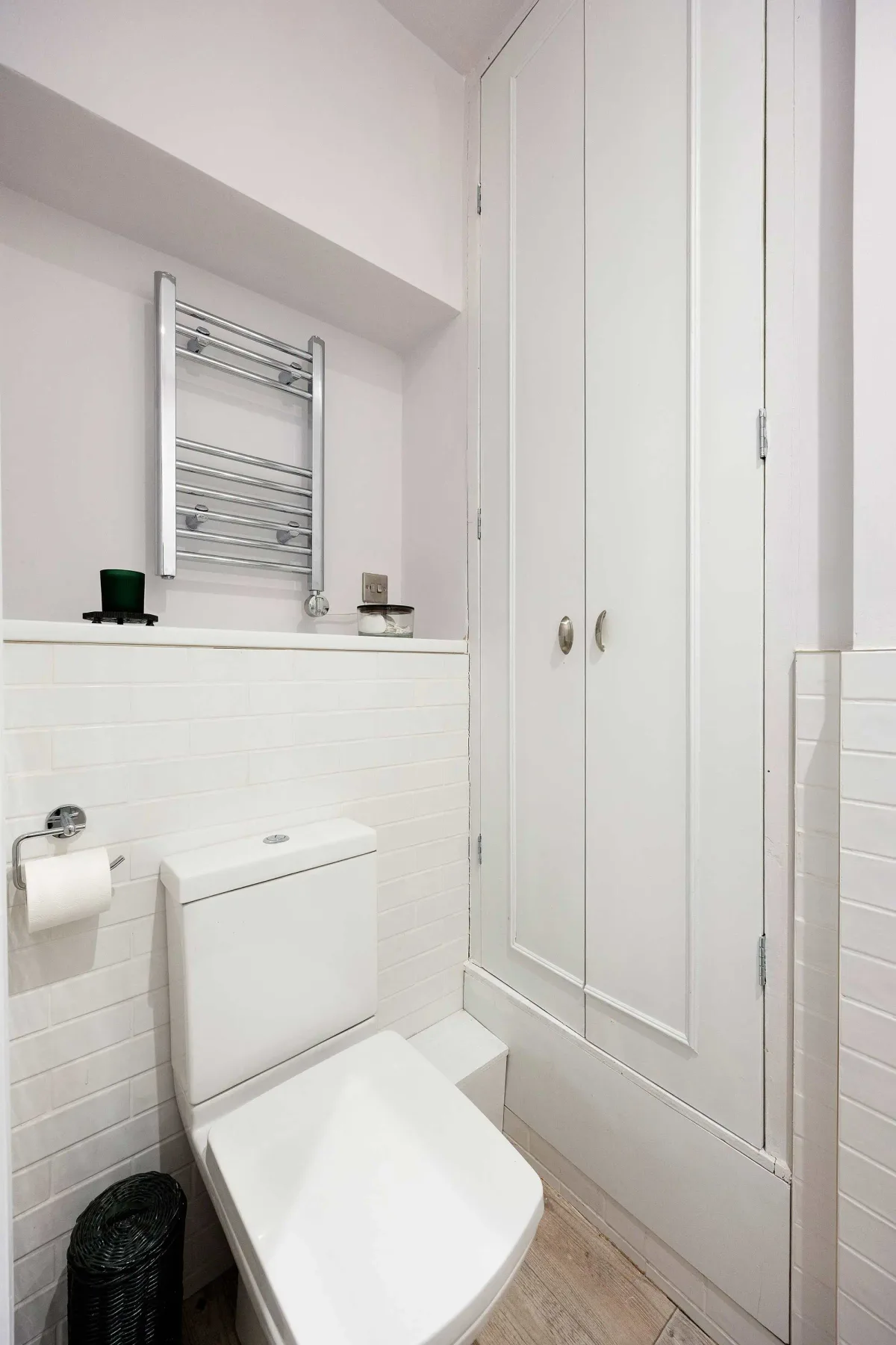 A compact bathroom with a toilet, wall-mounted towel rail, and built-in storage.