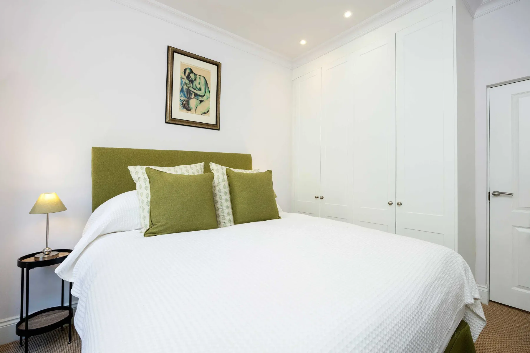A bedroom with a white bed and olive-green headboard and pillows.