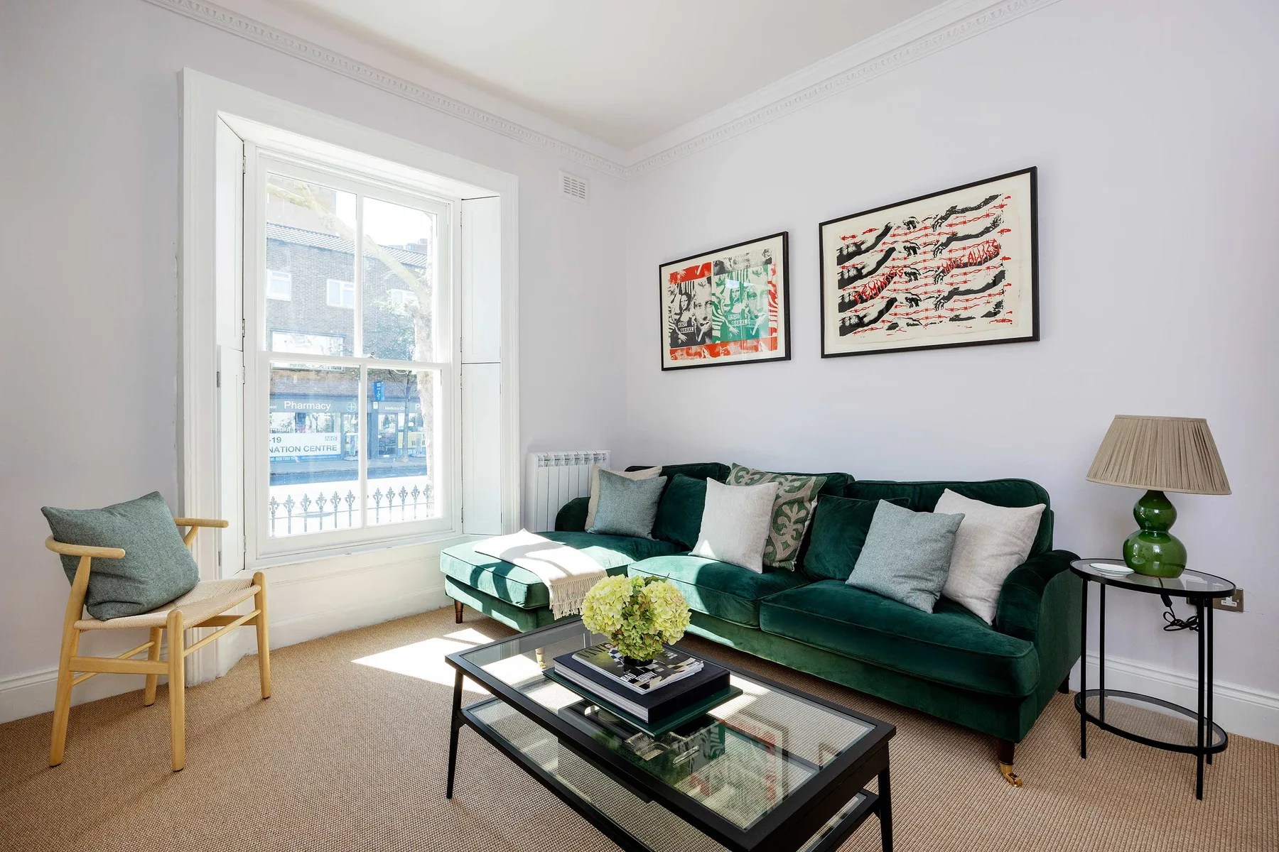 A bright living room with green seating, a large window, and framed artwork.