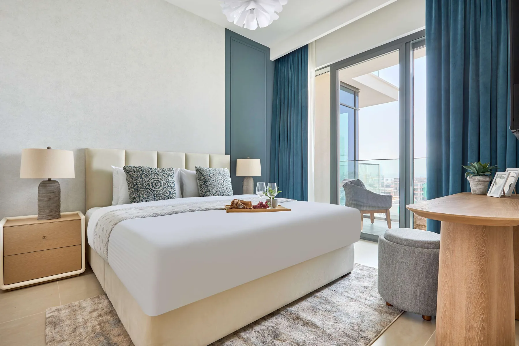 A bedroom with a bed, blue curtains, and a glass door opening onto a balcony.