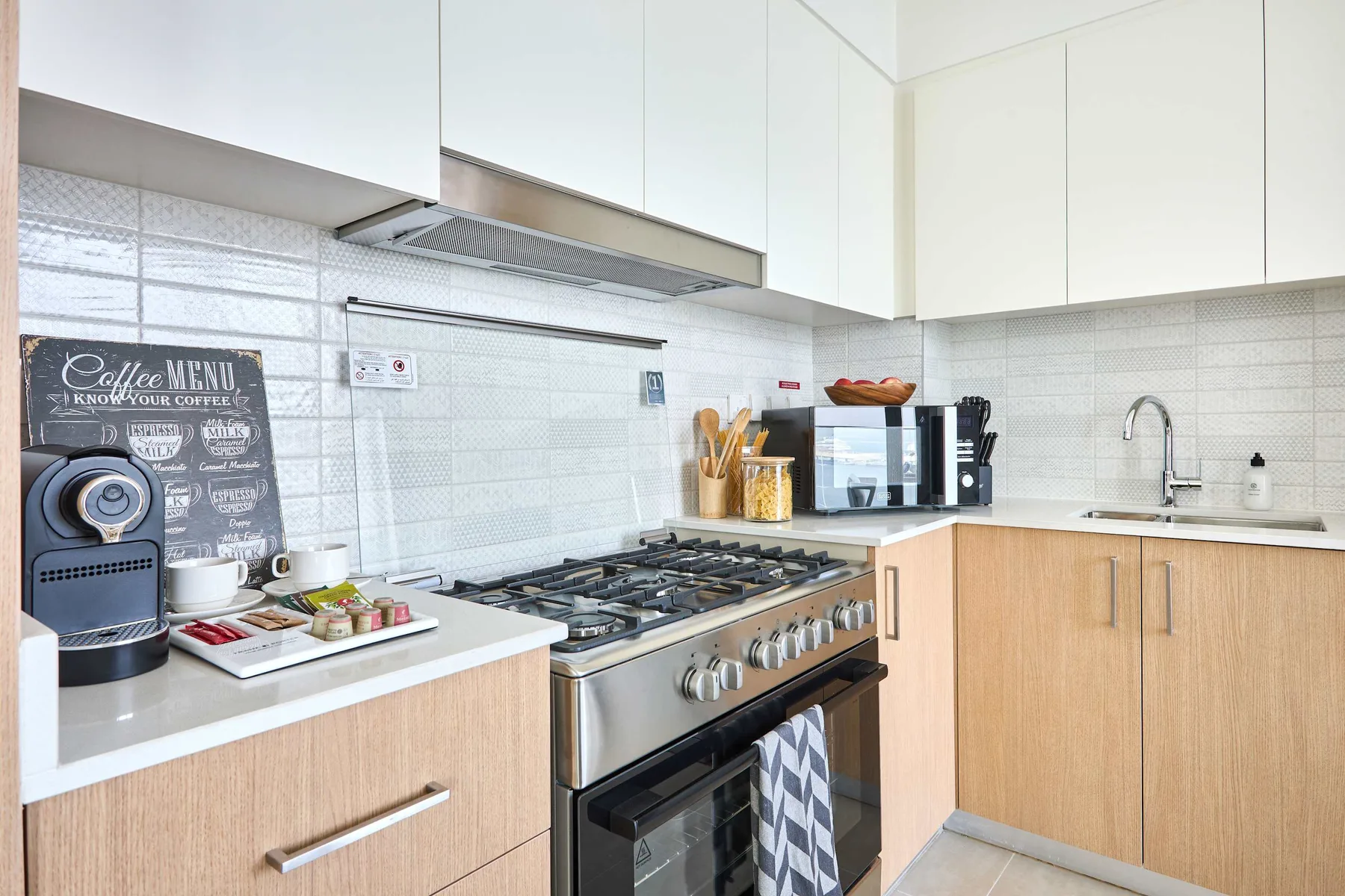 A bright kitchen with a stainless steel range, countertop appliances, and light wood cabinets.