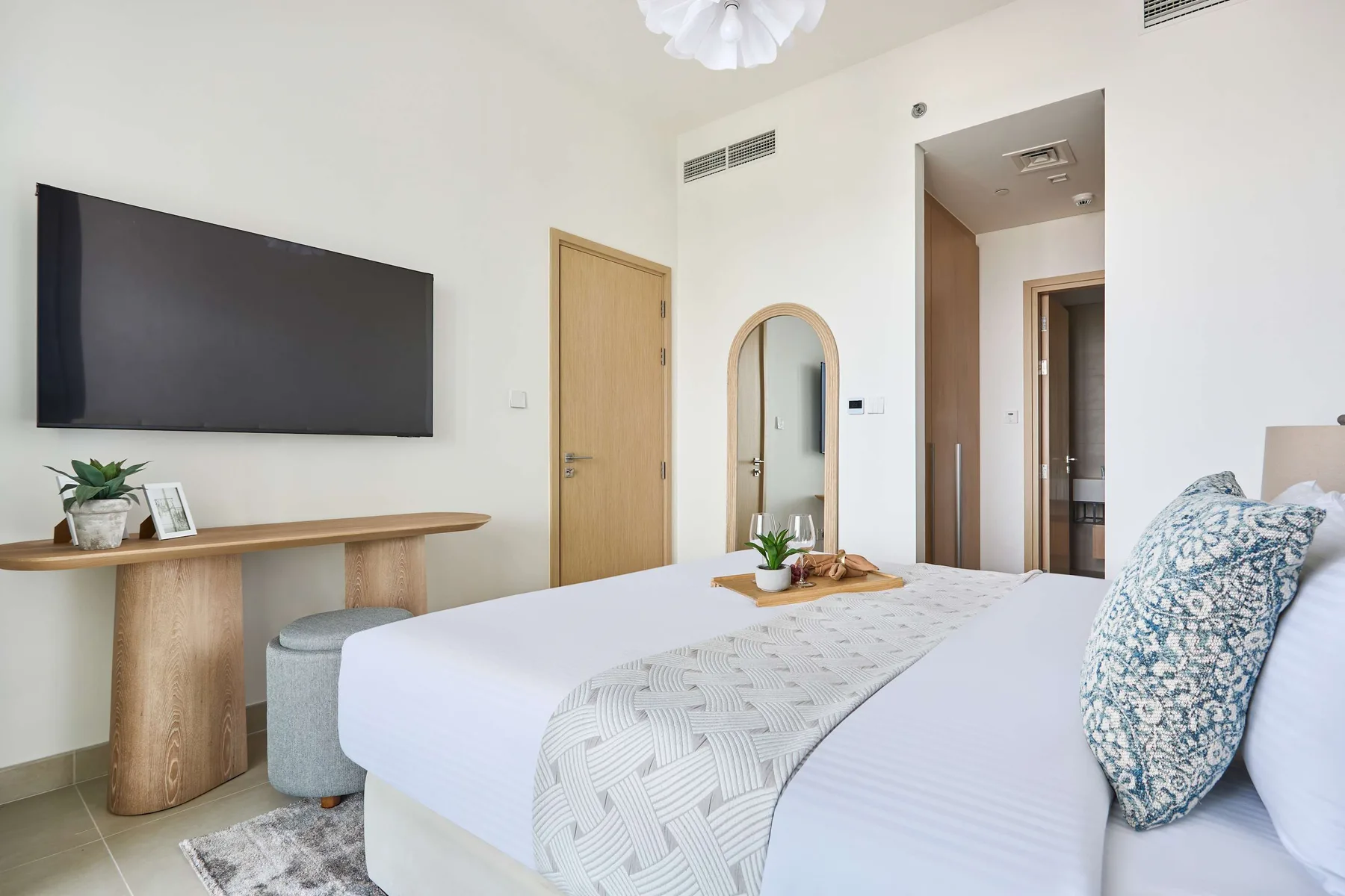 A bright bedroom with a neatly made bed and a wall-mounted television.