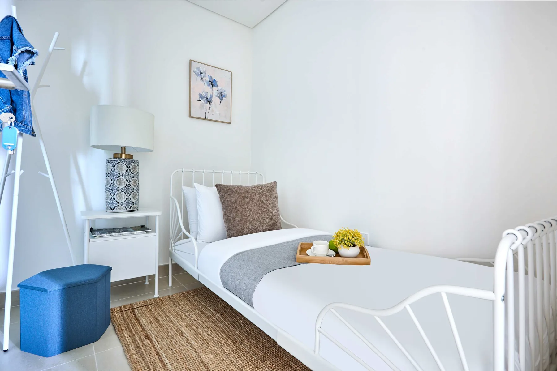 A bright bedroom with white beds, a bedside table, and a blue storage stool.