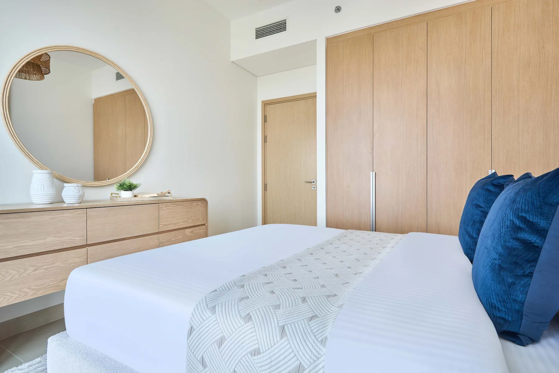 A bright bedroom with a bed, blue pillows, and a light wood dresser.