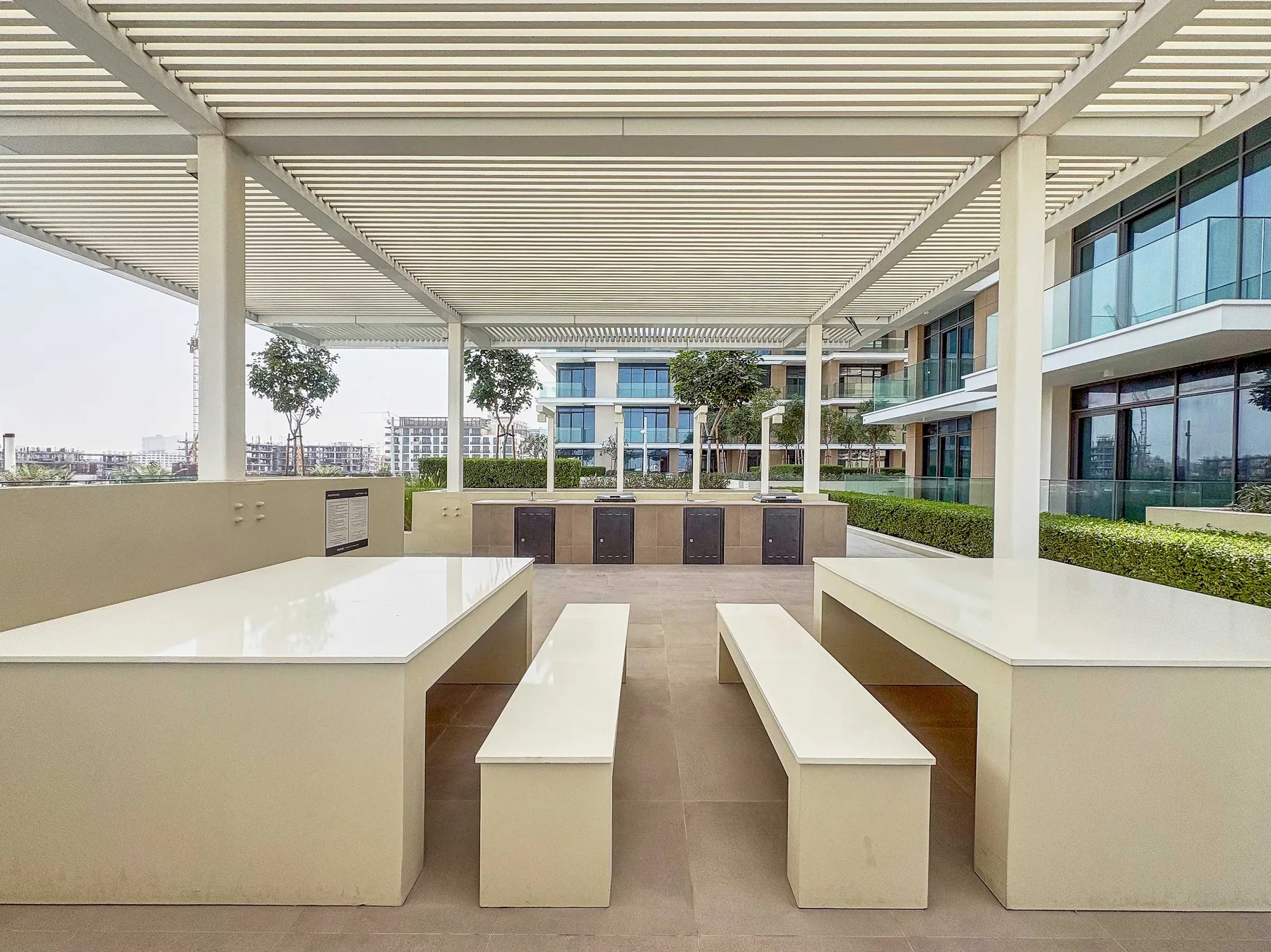 A covered outdoor dining area has long tables and benches beneath a slatted roof.