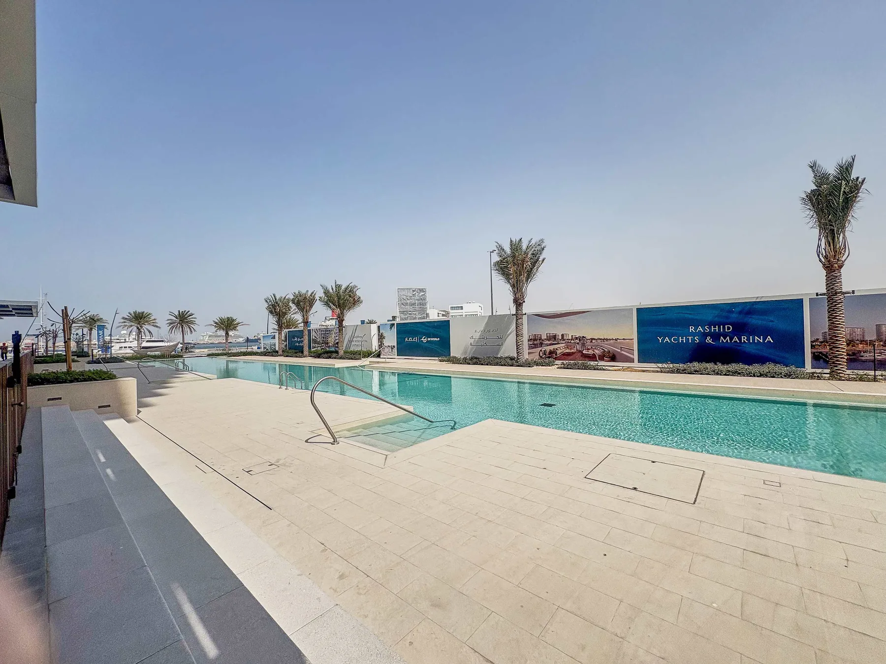 An outdoor swimming pool beside a paved deck and palm trees.