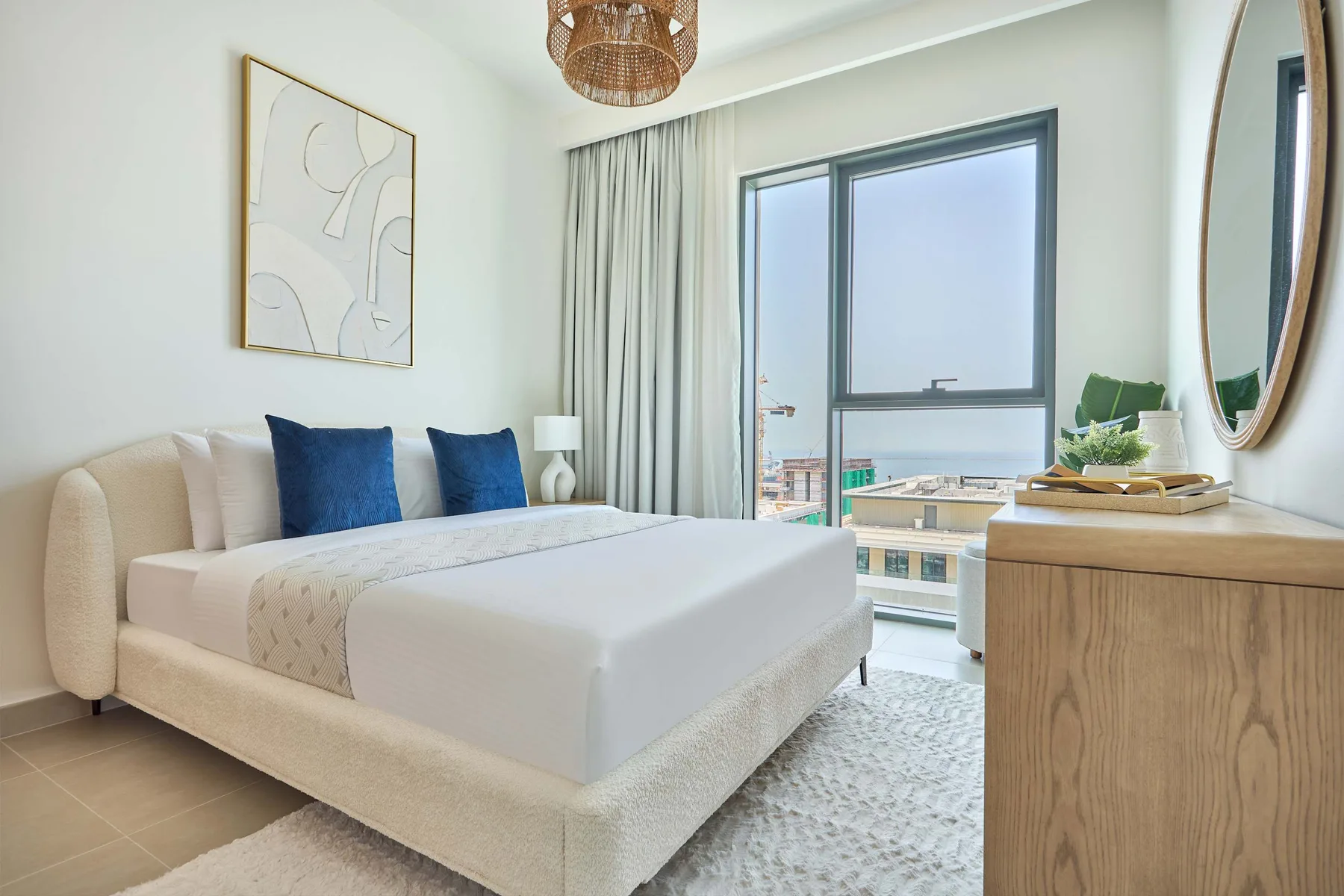 A bright bedroom with a neatly made bed beside a large window.