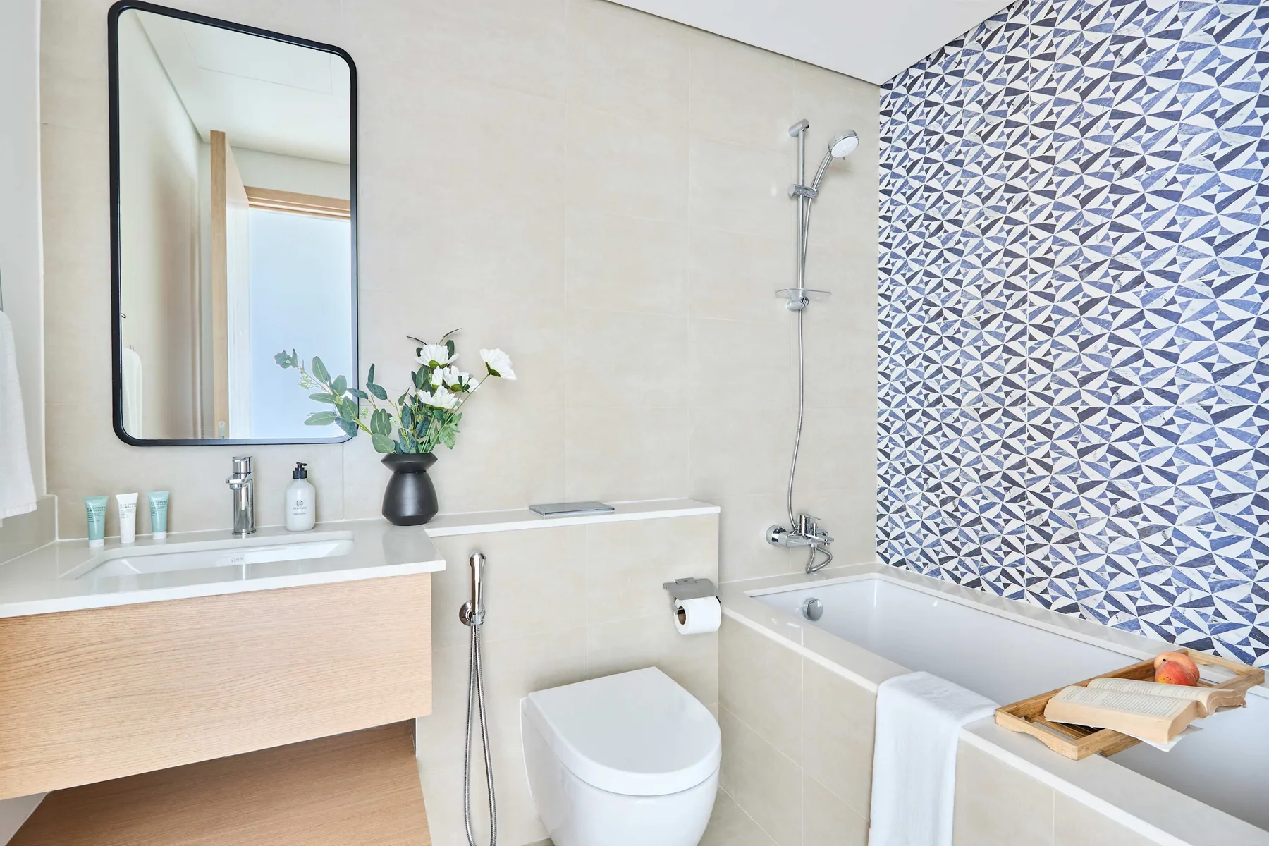 A bright bathroom with a sink, toilet, and bathtub beside patterned tile.