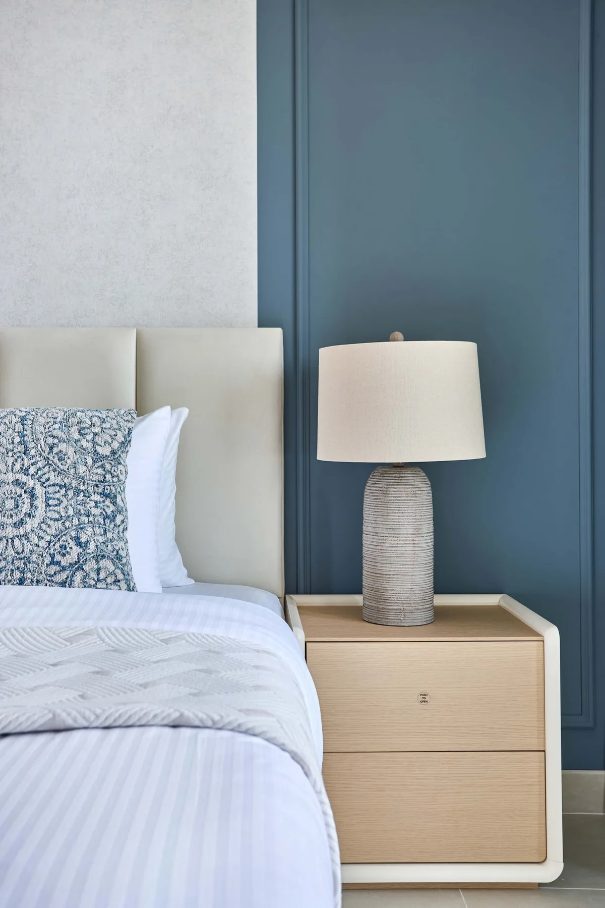A bedroom with a neatly made bed beside a bedside table and lamp.