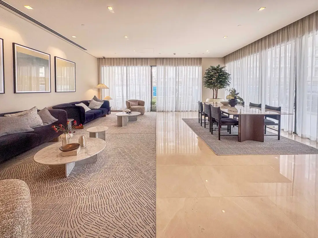 A bright living and dining area with seating, a dining table, and large curtained windows.