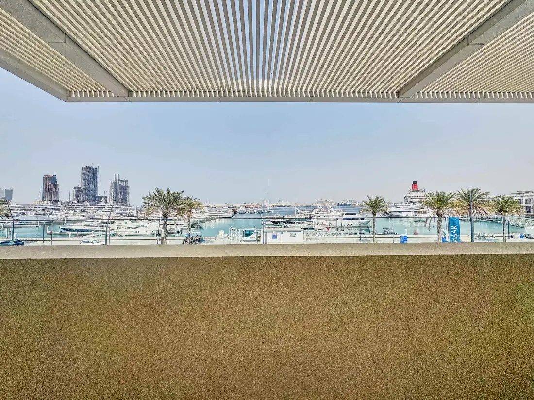 A shaded balcony overlooks a marina with boats and palm trees.