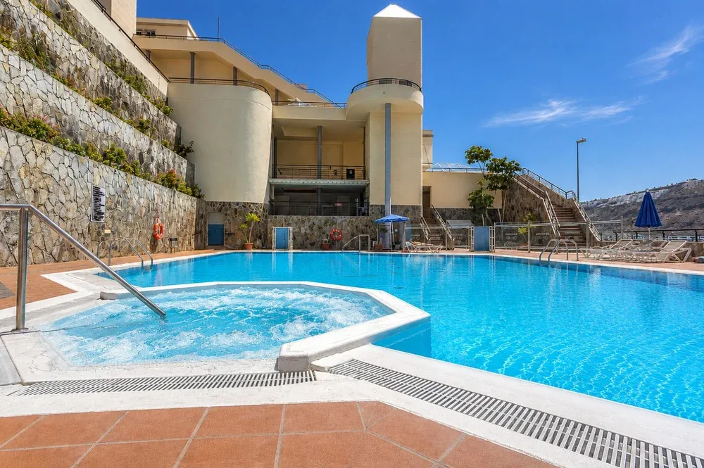 Una piscina al aire libre junto a un edificio moderno y un muro de contención de piedra.