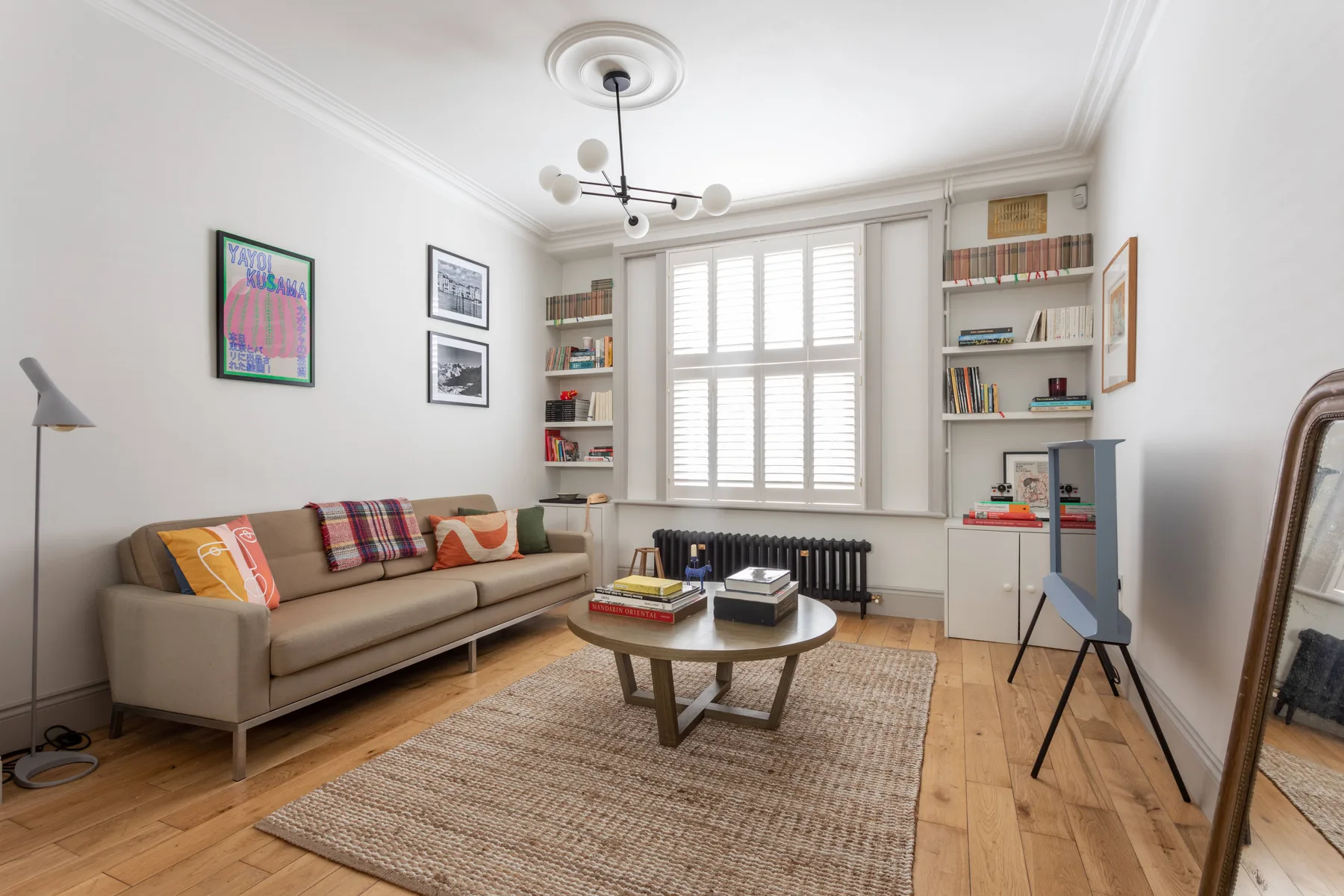A bright living room with seating, a coffee table, and a large shuttered window.