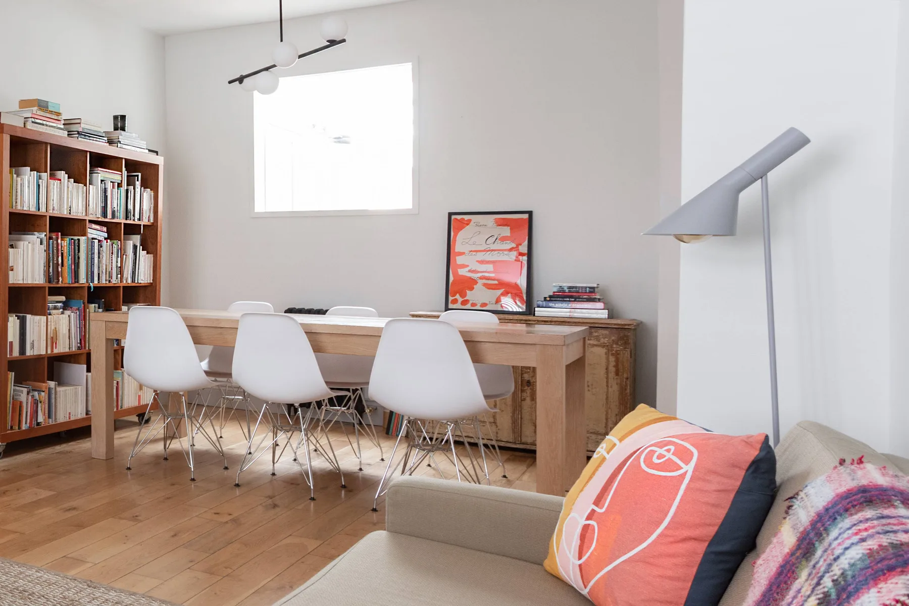 A bright dining and reading area features a wooden table, bookshelves, and seating.