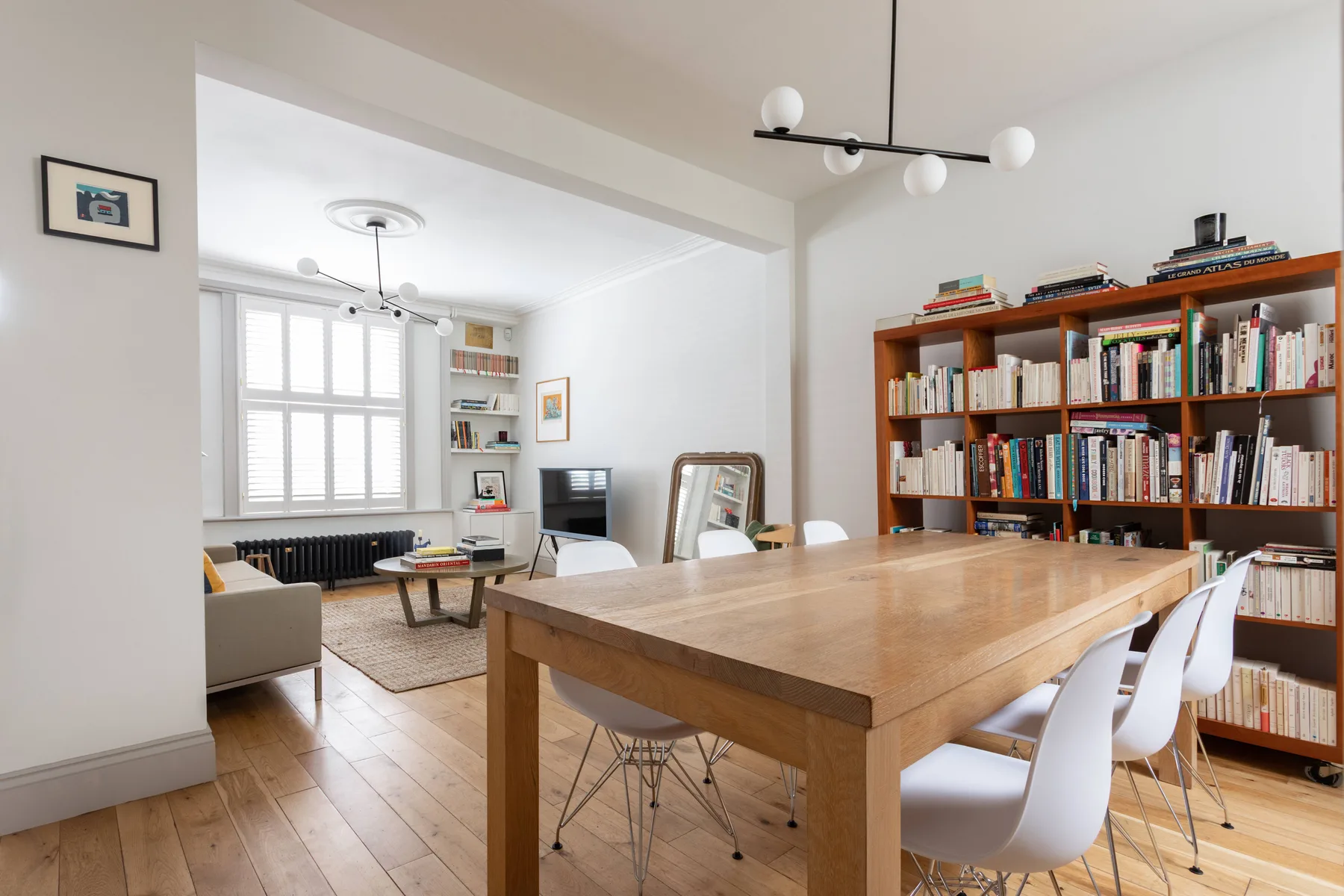 A bright dining and living area with a large wooden table and bookshelves.