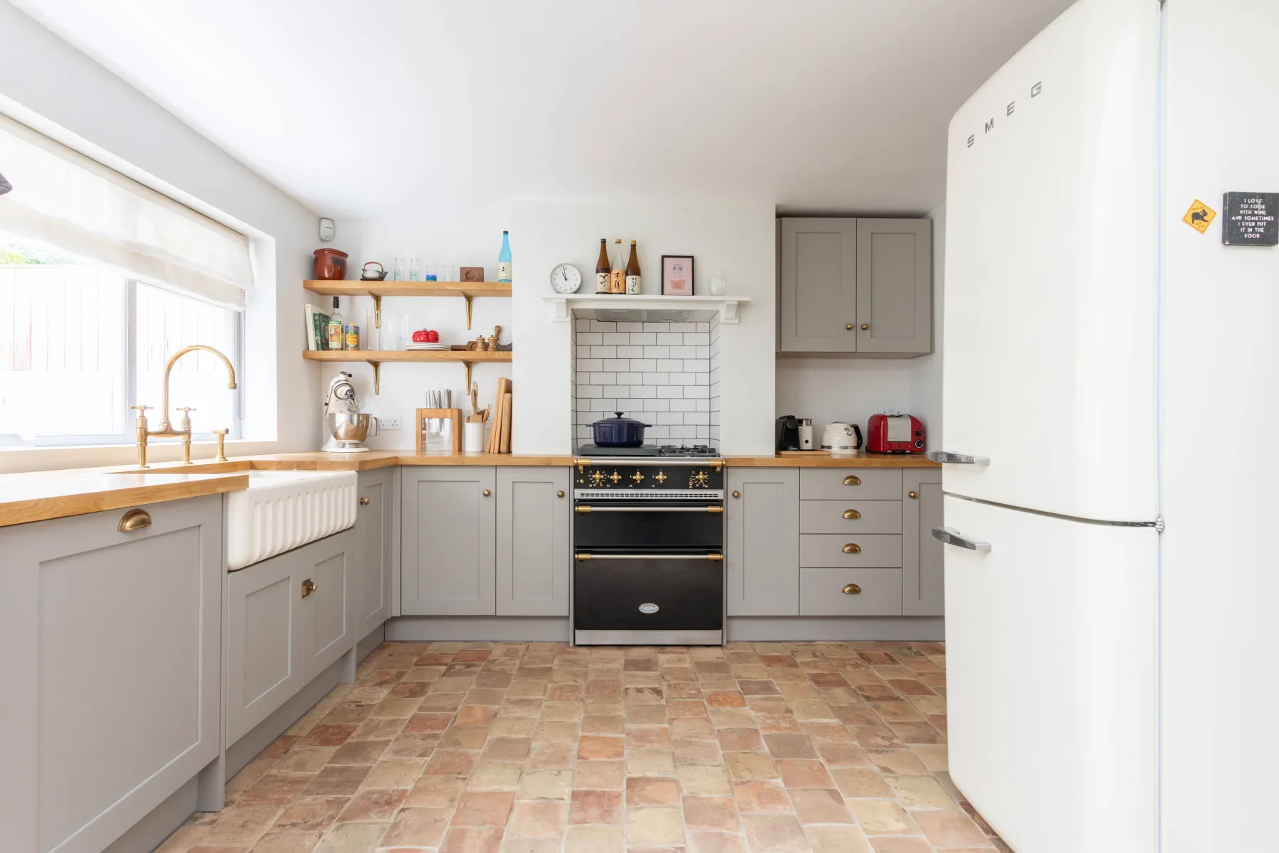 A bright kitchen with gray cabinets, a tiled backsplash, and a large refrigerator.